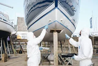 Two workers applying an underwater hull coating to a yacht ashore