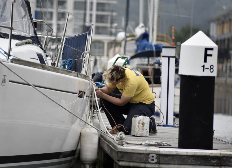 A person attending to a sailing yacht alongside a marina pontoon