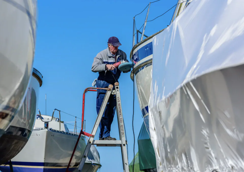 A person polishing the hull of a yacht ashore