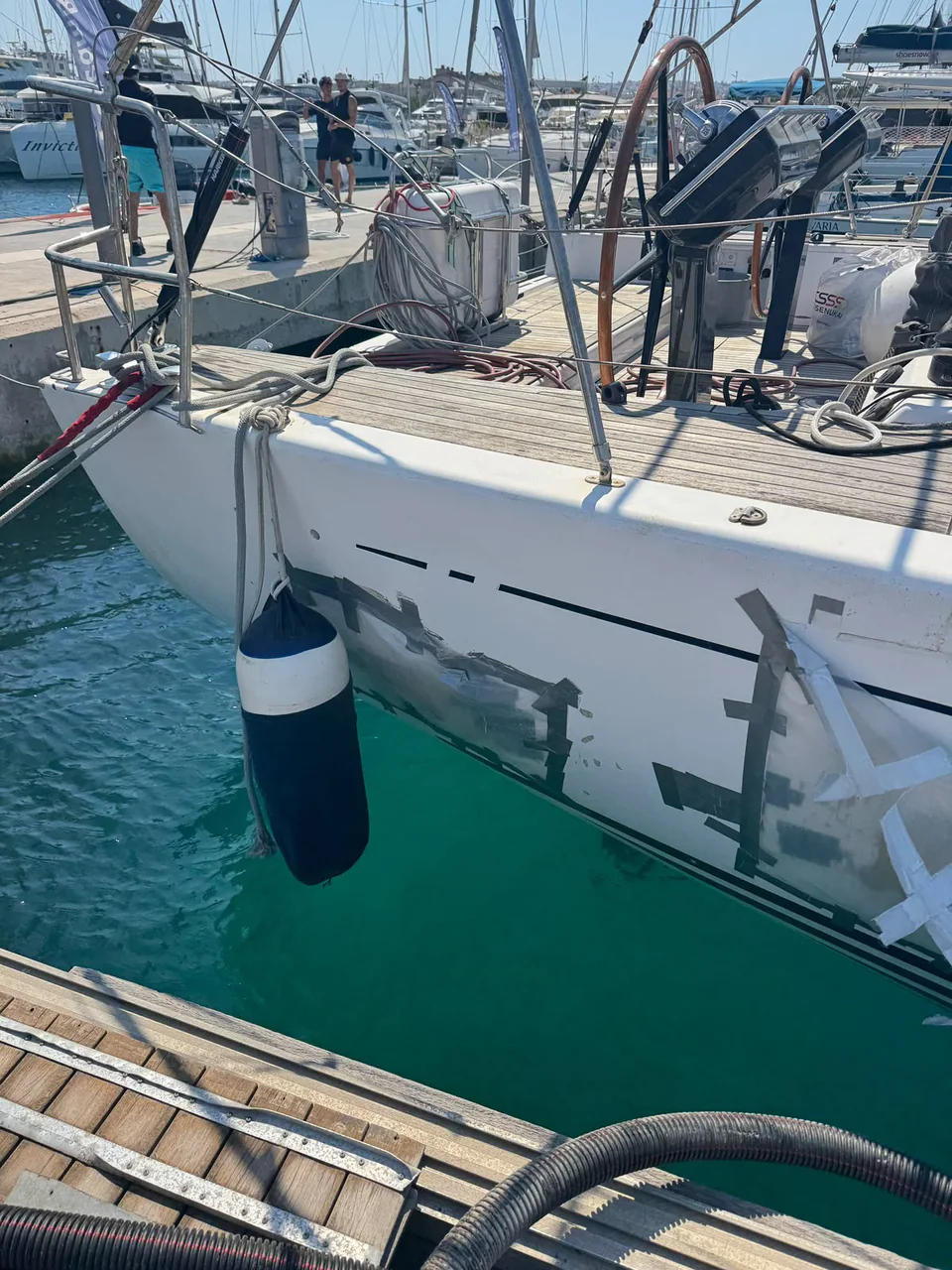 Sailing yacht with visible hull damage and temporary covering at a marina